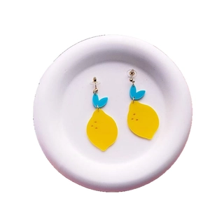 Yellow lemon acrylic earrings with blue leaf accents on a white decorative dish