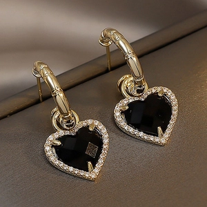 Close-up of golden bamboo hoop earrings with black heart charms and sparkling crystals