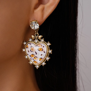 Close-up of heart-shaped leopard print earrings with sparkling rhinestones on model