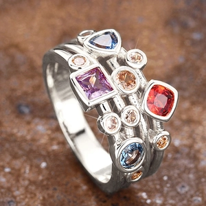 Vista macro de un anillo geométrico multicapa con gemas de colores y acabado plata