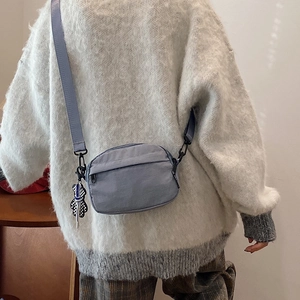 Minimalist grey-blue nylon crossbody bag with checkered charm shown on model