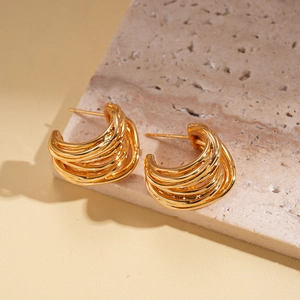Detail of gold plated geometric spiral earrings on beige stone with texture