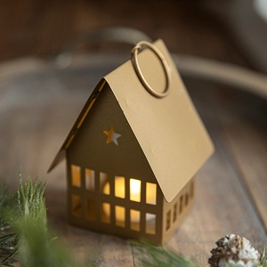 Golden house-shaped iron candle holder with star cutouts on wood tray with pine cones