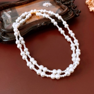 Double-layered white pearl necklace with gold clasp on vintage dark red leather background