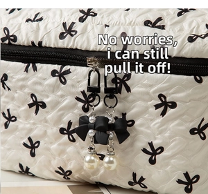 Close-up of white quilted cosmetic bag with black bow charms and pearl zipper details