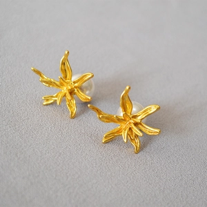 Detailed macro view of gold-plated lily flower earrings with white pearl centers