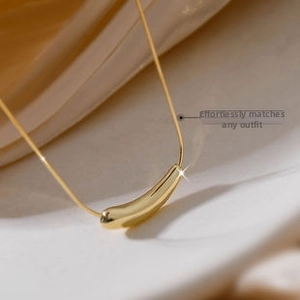 Macro shot of mirror-polished gold bean pendant on a fine snake chain necklace