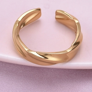 Macro detail of gold irregular twisted stainless steel ring on soft pastel background