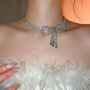 Detail of silver bow necklace with rhinestones and pearls on model in white feathers