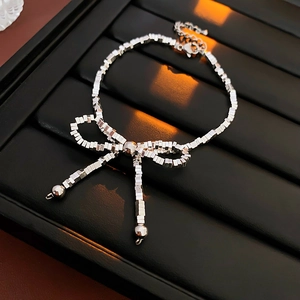 Detail of silver bow bracelet with small square links and bead tassel drops on black tray
