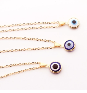 Detailed view of three gold evil eye necklaces with colorful resin enamel pendants