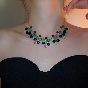 Close-up of gold necklace with green and blue teardrop gems worn on a neck