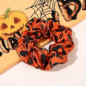 Close-up of Halloween scrunchie with pumpkin and skull patterns on glossy satin fabric