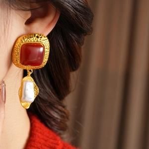 Close-up of vintage baroque pearl earrings with red resin and hammered gold metal finish