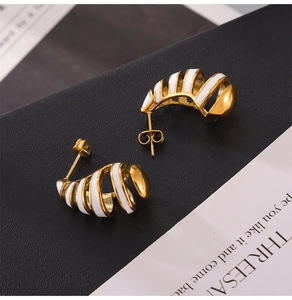 Macro shot of geometric gold and white enamel drop earrings on black leather base