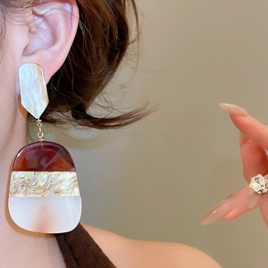 Detailed close-up of acetate resin oval drop earrings in brown and beige on model