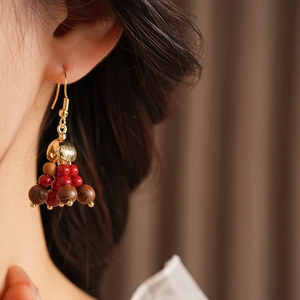Detail of bohemian wooden bead earrings with red glass accents and golden hooks on model