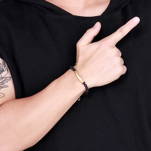 Detail of men's matte black onyx beaded bracelet with curved gold metal tube on wrist