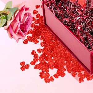 Macro view of red glitter heart sequins with metallic shredded paper in a gift box