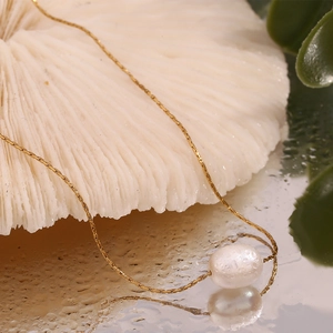 Detail of a natural white baroque pearl on a thin gold stainless steel chain