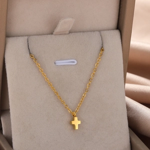 Detail view of a gold cross pendant on a delicate chain in a velvet jewelry box