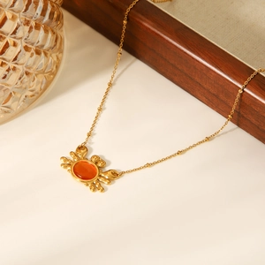 Macro shot of crab pendant with orange opal stone on a gold beaded chain necklace