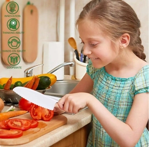 Close-up of a child using a serrated plastic safety knife to cut a fresh tomato