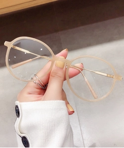 Details von runder cremefarbener Brille mit schmalen goldenen Metallbügeln in der Hand