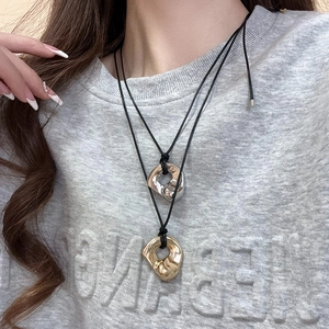 Close-up of liquid metal heart pendants in gold and silver on black cord necklace