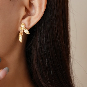 Detailed close-up of a gold metal bow earring with handcrafted brushed texture on model