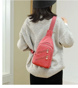 Close-up of pink nylon crossbody chest bag with multi-zipper pockets shown on a model