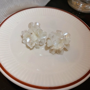 Elegant white acrylic flower cluster stud earrings on a ceramic dish with soft lighting