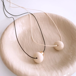 Detail of minimalist resin bead pendant on wax cord over a beige ceramic tray