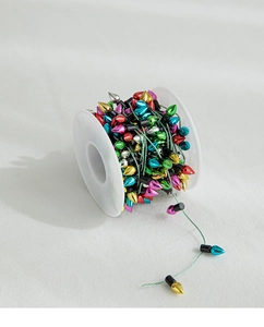 Close-up of colorful Christmas bulb beaded string with metallic finish on a white reel