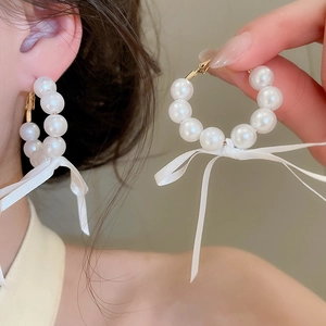Detail view of French style pearl hoop earrings with delicate white ribbon bows
