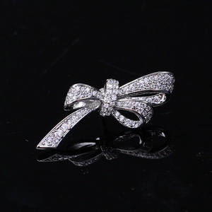 Detail of silver bow brooch with pavé cubic zirconia on reflective black surface