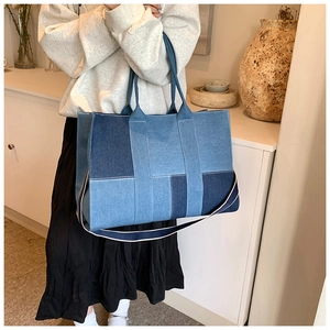 Detail of blue patchwork denim tote bag with white stitching and wide shoulder strap