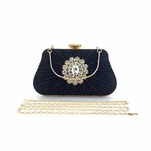 Macro view of black pleated satin evening clutch with rhinestone floral ornament and gold chain