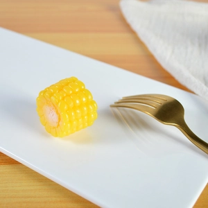 Realistic yellow corn food model on white plate with gold fork on a wooden table