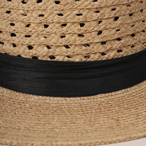 Close-up detail showing the hand-woven raffia texture and black ribbon band of this summer hat