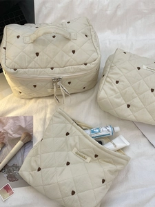 Beige quilted makeup bag set with brown hearts on soft white bedding for travel