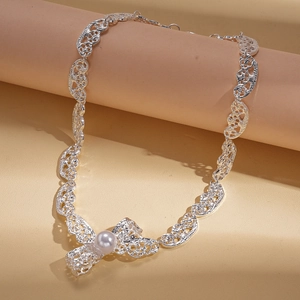 Silver hollow lace necklace with white pearl on beige display stand in warm lighting