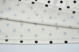 Macro shot of white fabric with black polka dots showing double-needle stitching detail
