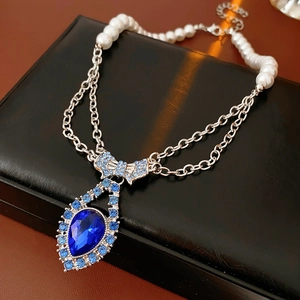 Macro detail of a pearl necklace featuring a blue gemstone pendant with a silver bow