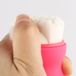 Dual-sided facial cleansing brush with soft white bristles and pink handle shown in detail