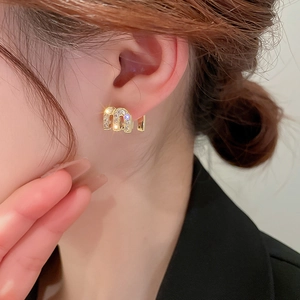 Close-up of golden letter M earrings with zircons on a female model wearing a black blazer
