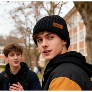 Close-up of black ribbed knit beanie with brown leather logo patch worn by male model