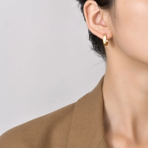 Close-up of small gold hoop earrings with white zircons worn on a female model