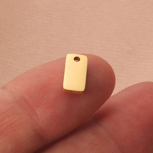 Polished gold rectangular stainless steel pendant held on finger tip for DIY jewelry making