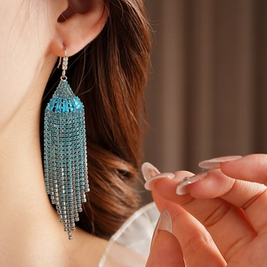 Macro shot of long blue tassel earrings with sparkling rhinestones worn by a model